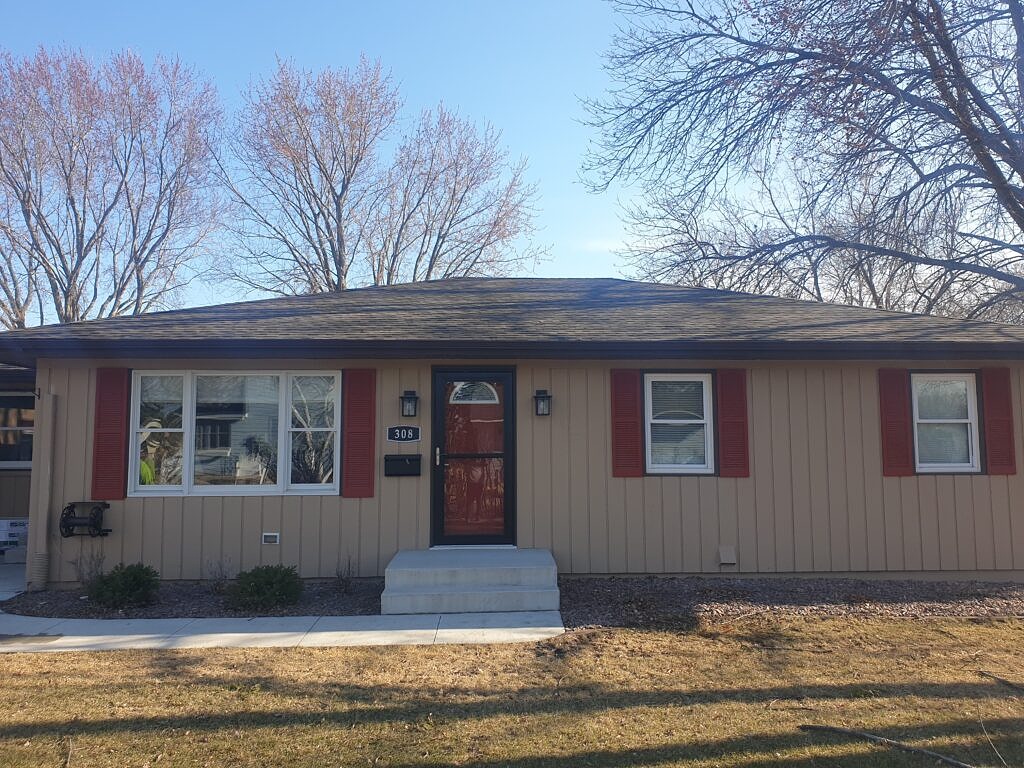 House with tan siding and a teak colored roof.