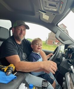 Picture of JT with his boy on his lap behind the wheel of a pickup truck
